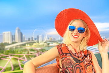Happy lifestyle caucasian woman in wide hat enjoying cityscape skyline. Blonde tourist above aerial view of Singapore marina. Travel holiday vacation in Singapore, Southeast Asia. Sunny day, blue sky.