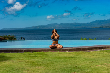Filipina girl doing yoga poses poolside with ocean background