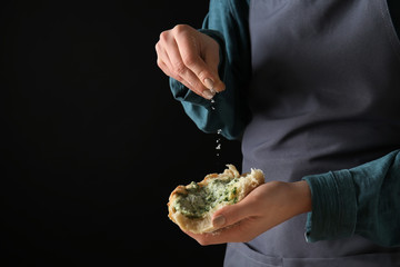 Young woman sprinkling cheese onto piece of fresh bread with green butter against dark background