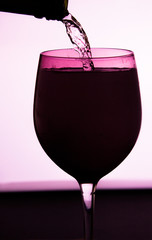 Bottle wine is pouring to glass, pink color glass, white background, dark green bottle
