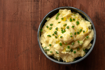 Pomme puree, a photo of a bowl of mashed potatoes with scallions, shot from the top on a dark rustic background with a place for text