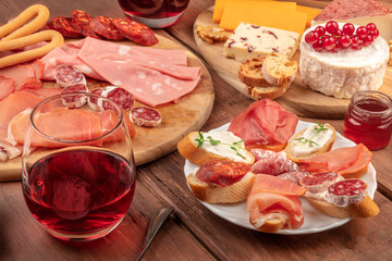 Wine tasting and pairing. A wineglass with charcuterie, sandwiches and a cheese platter on a dark wooden background