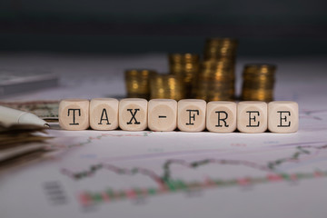 Word TAX-FREE composed of wooden letter. Stacks of coins in the background.