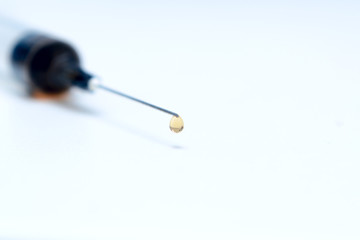 There is a drop of medicine on the point of the needle of the syringe