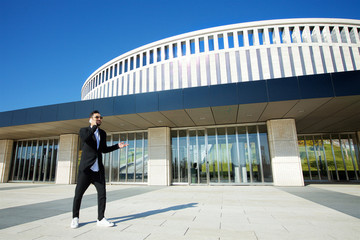 A successful representative of a rich and fashionable man with a beard standing on the street in front of a modern building.