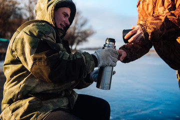 Fisherman pours tea from a thermos in the winter on the ice. Winter fishing