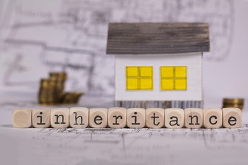 Word INHERITANCE composed of wooden letter. Small paper house in the background.