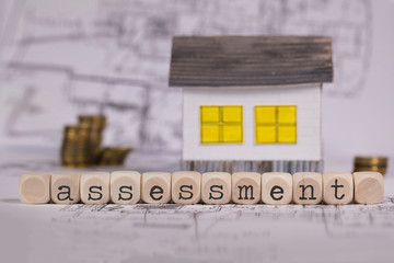 Word ASSESSMENT composed of wooden letter. Small paper house in the background.