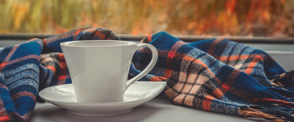 Cozy autumn still life: a mug of hot coffee and an open book with a warm blanket on the old window...