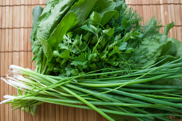 Spring onions, spinach leaves, dill and parsley on a wooden bamboo background. Top flat lay view.