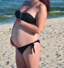 a pregnant woman poses for a photographer at the sea, her face is not visible, her hands on her stomach