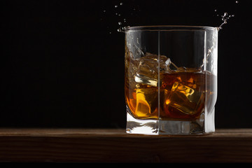 Glass of whiskey with ice cubes on a wooden table and dark background.