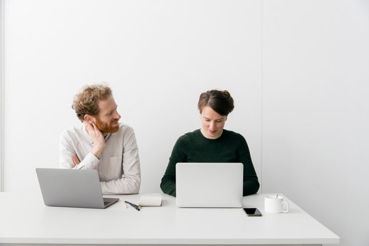 A thirty something couple is working on a laptop in a clean white empty office setting.