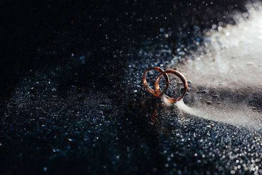 Wedding rings on dark surface shining with light close up macro. Water splashes. Reflection. Lights and smoke.