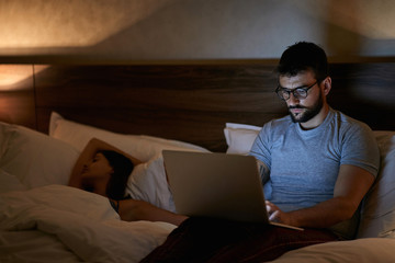 Businessman lying on bed and working with laptop late at night..