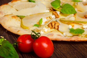 Fototapeta na wymiar Vegetarian Italian pizza with nuts, yellow pear, parmesan cheese and fresh green basil leaves on a brown table decorated by mozzarella, red hot chili pepper, cherry tomatoes
