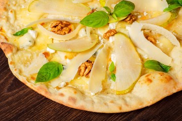 Vegetarian Italian pizza with nuts, yellow pear, parmesan cheese and fresh green basil leaves on a brown table decorated by basil leaves. Top view. Close up.