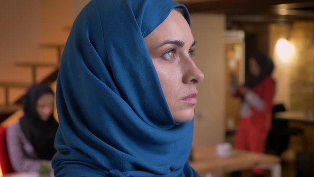 Closeup portrait of young beautiful muslim female in blue hijab turning from the side and looking straight at camera