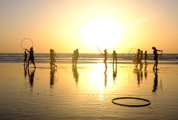 Girls with hula hoops on the ocean beach at sunset background