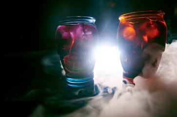 two glasses in the form of skulls of different colors, stand next to each other in the smoke