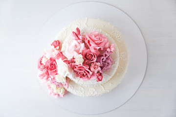 Two-tiered white wedding cake decorated with pink flowers on a white wooden background. Top view.