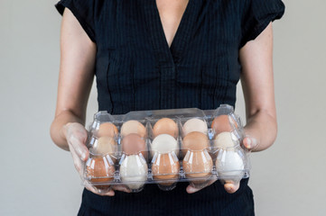 Caucasian woman with black shirt holding a plastic egg box full of chicken eggs