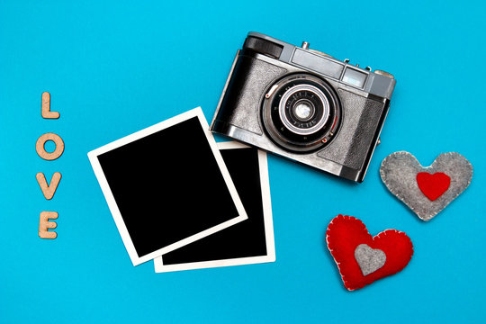 Vintage camera with two felt hearts and photo cards. Top view on blue background