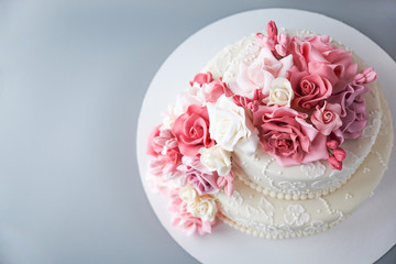 Two-tiered white wedding cake decorated with pink flowers on a gray background. Top view. Cutout.
