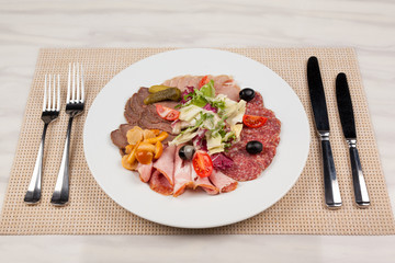 Sausage and meat with vegetables on a white plate with cutlery on the table.