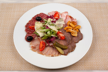 Sausage and meat with vegetables on a white plate with cutlery on the table.