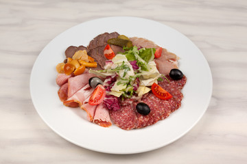 Sausage and meat with vegetables on a white plate with cutlery on the table.