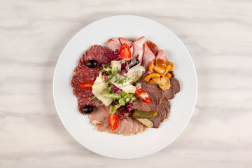 Sausage and meat with vegetables on a white plate with cutlery on the table.