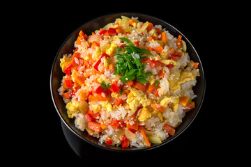 A plate of delicious rice with scrambled eggs and vegetables: carrots, sweet peppers, greens, spices and sauce on a black background