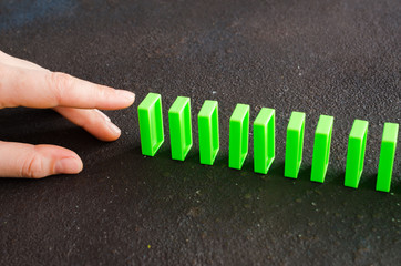 Hand ready to push domino piece to cause chain reaction.