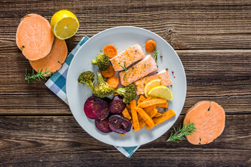 Baked salmon with vegetables. Cooked fish fillet with fries on plate, top view