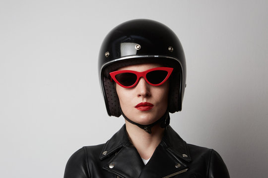 Headshot Portrait of fashion girl with red lips in black leather jacket wearing sunglasses looking at camera over white background. Fashion, glamour and transportation concept