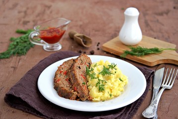 A meatloaf with mushrooms and red sweet pepper on a white plate with a garnish of mashed potatoes. Selective focus.