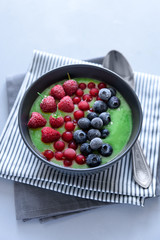 Breakfast kiwi smoothie bowl topped with frozen raspberry, blueberry and red currant on gray wooden...