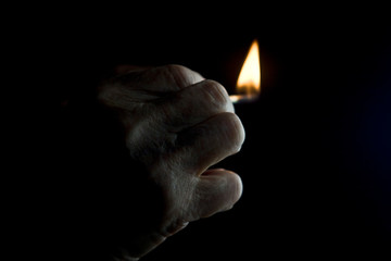 Burning match in old hand on dark background close up