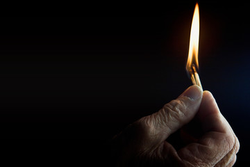 Burning match in hand on dark background