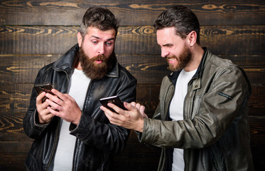 Men brutal bearded hipster in fashionable leather jackets use mobile internet. Online business. Modern technology. Men with smartphones surfing internet. Mobile internet. Business application