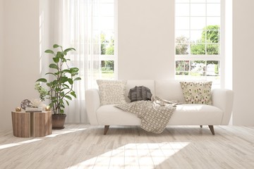 Fototapeta premium White stylish minimalist room with sofa and summer landscape in window. Scandinavian interior design. 3D illustration