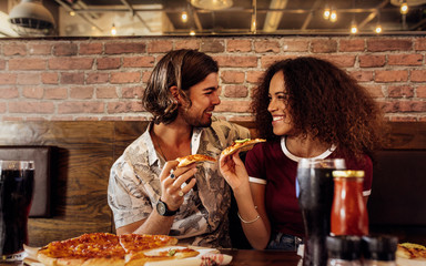 Couple enjoying eating pizza at cafe.