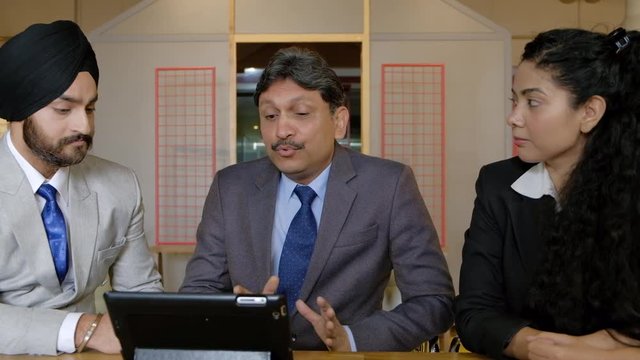 Indian office with a senior management guy telling and explaining his juniors work on a portable tablet technology communication device with internet over wifi in a causal working space