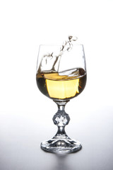 White wine splashing in wine glass on light background. .