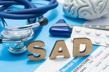 SAD medical abbreviation meaning seasonal affective disorder, depression could during seasons with little light. Word SAD is surrounded by stethoscope, result of mental status exam, drugs and brain