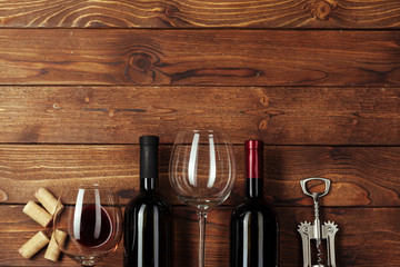 Red wine bottle, wine glass and corkscrew on wooden table background