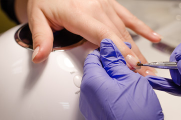 Closeup shot of master in rubber gloves covering nails with base gel in the beauty salon. Perfect nails manicure process