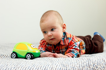 The baby boy is playing with a green little car plaid shirt