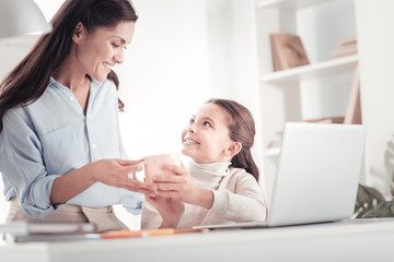 Caring tender mother bringing daughter cup of tea to her child room